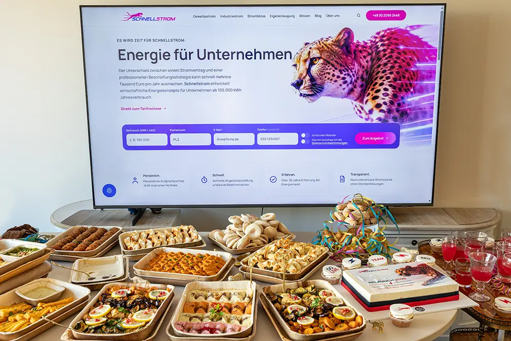 Großer Bildschirm mit der Startseite des neuen Schnellstrom-Auftritts, davor ein Buffet mit Fingerfood, der Relaunch-Torte und Cupcakes